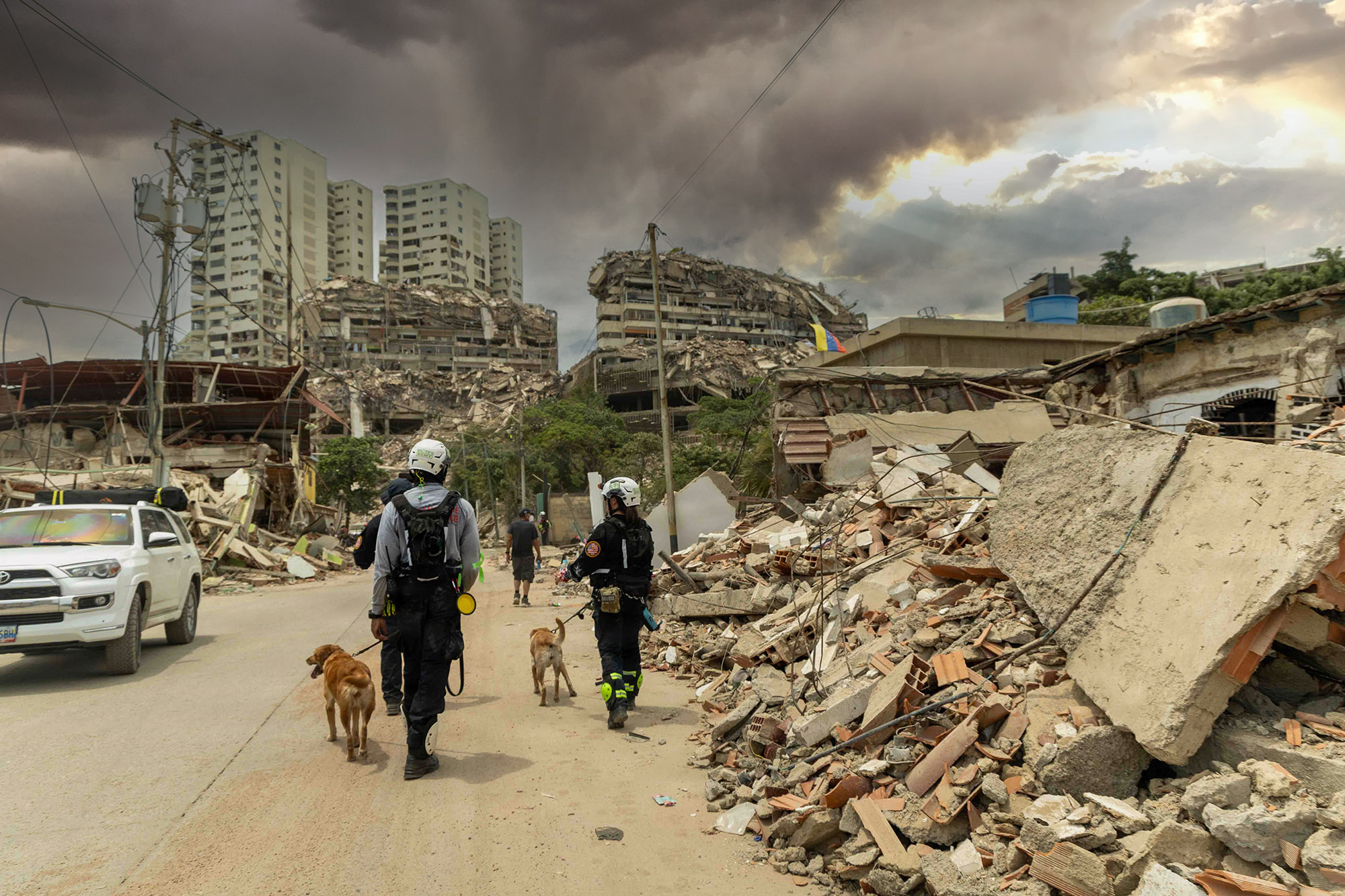 Rescatistas con perros de búsqueda caminan por una calle con edificios derrumbados por los terremotos en Venezuela