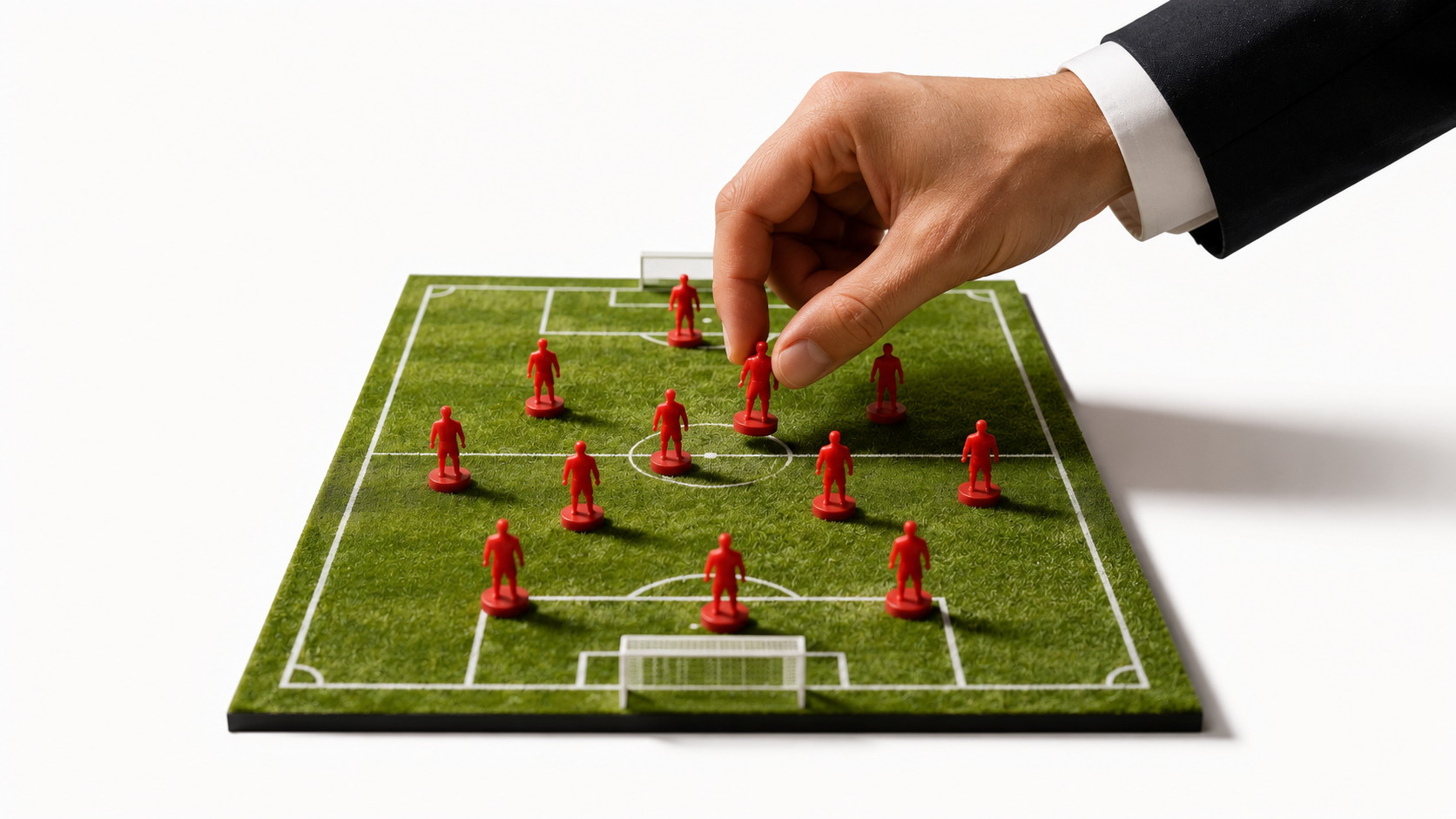 Una mano con traje coloca figuras rojas de futbolistas sobre un campo de fútbol en miniatura